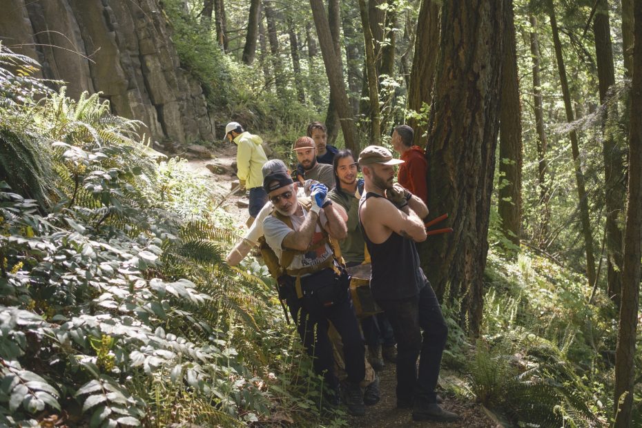 A group of five climbers moving a single large rock to make steps.